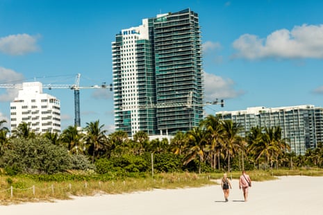 Two people walk on a beach, large condo buildings in the background