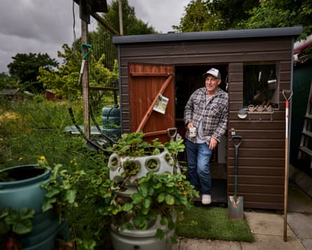 Alan Hodson holds a mug of tea as he stands in the doorway to his shed with pots and plants around it