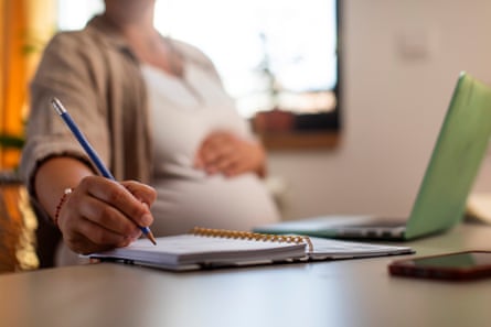 A pregnant woman holding her stomach and taking notes on a notepad