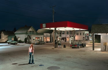 a woman looking up while standing in front of a gas station at night