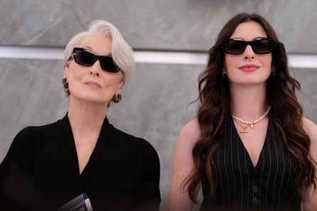 The two women, both dressed in black and wearing dark glasses, stand side by side staring ahead