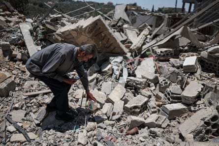 A man bends down to pick something up from the rubble of a destroyed building