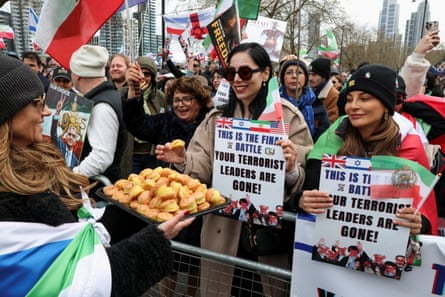 A woman hands out sweets to counterprotesters who are holding notices in support of the war on Iran