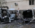 A woman walks past two burnt-out cars