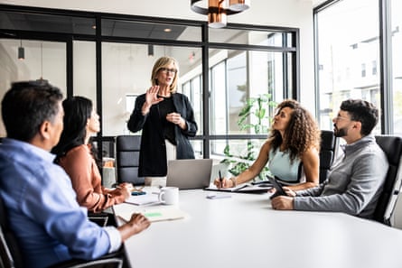 Business colleagues meeting in a modern conference room where a blond woman with glasses is giving a presentation.