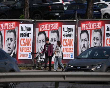 A couple walks in front of pro-government billboards featuring portraits of Ukraine's President Volodymyr Zelenskyy and Hungarian opposition leader Peter Magyar in Budapest, Hungary.