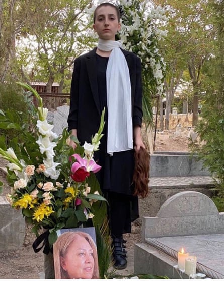 An Iranian woman stands by the grave of her mother, Mino Majidi, killed in the protest movements. The woman’s head is shaved and uncovered, and in her hand she holds the hair she shaved off in protest at both deaths.