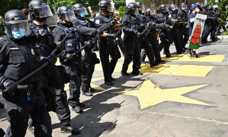 A line of police officers in riot gear move forward to form a security perimeter on 16th St NW near Black Lives Matter Plaza and Lafayette Square near the White House in Washington on 23 June.