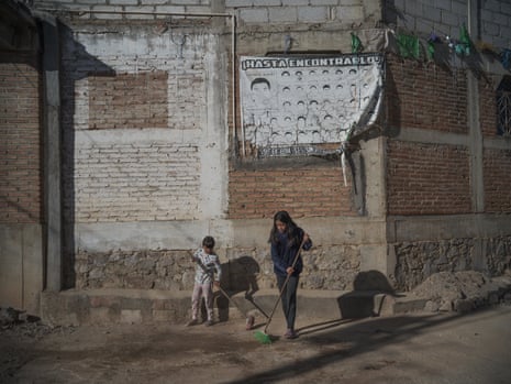 Joanna Hernández (8) and Yolsitlalin Hernández (11) sweep their street beside an old poster with the face of their uncle Benjamin and the other 42 students who disappeared eight years ago