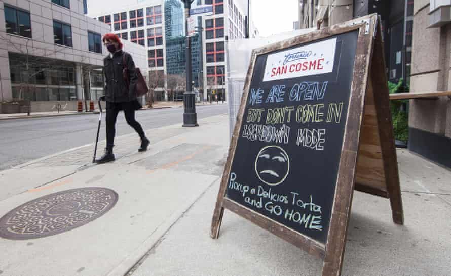 A woman wearing a face mask walks past a notice with words of “WE ARE OPEN BUT DON’T COME IN LOCKDOWN MODE” outside a restaurant in Toronto, Ontario