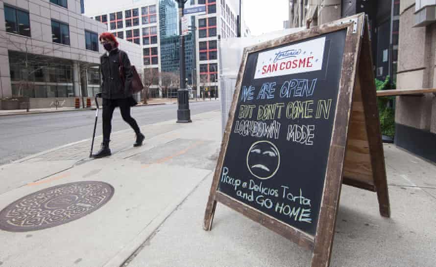 Une femme portant un masque facial passe devant un avis avec les mots «NOUS SOMMES OUVERTS MAIS NE VENEZ PAS EN MODE VERROUILLAGE» devant un restaurant à Toronto, Ontario