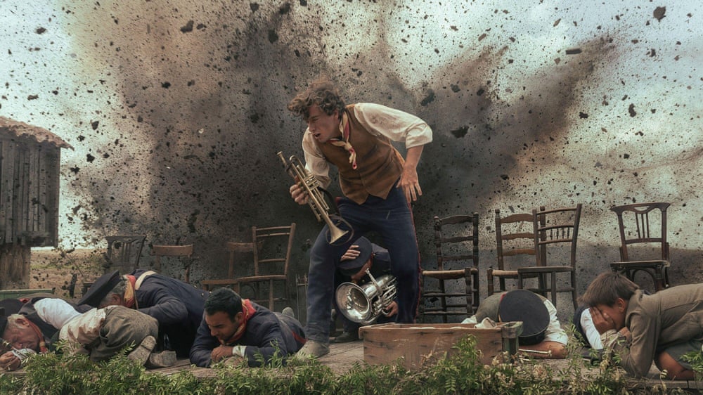 Guitarricadelafuente, holding a brass trumpet, shouts as an explosion occurs behind him and others around him hit the floor to protect themselves