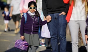 A child in purple school uniform holding a lunch bag