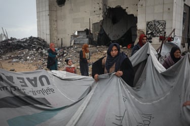 Displaced civilians in Gaza City hold up part of their shelter in a destroyed area