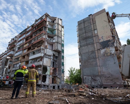 Men in hi-vis and helmets looking up at devastated blocks of flats.