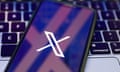 X logo on a phone that is resting against a laptop keyboard