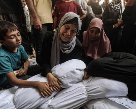 Two women and a child weep over two bodies wrapped in white sheets