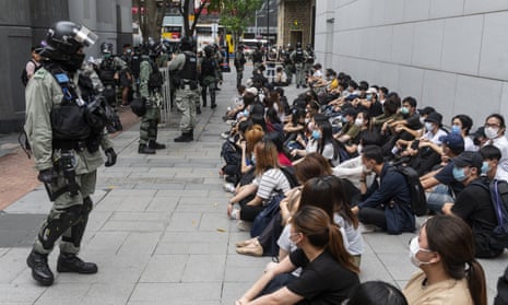 A large group of detainees sit on the ground as police officers set up a cordon in Hong Kong.