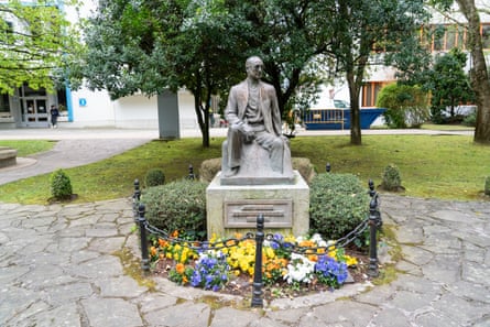 Statue of a seated José María Arizmendiarrieta. In front of the plinth are colourful flowers.