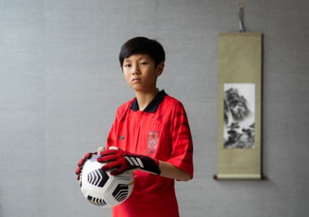 Noah Ji-Ha Shin holding a football and wearing goalkeeper’s gloves and a red South Korea shirt
