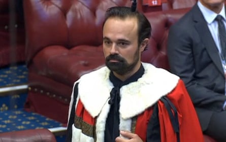 he is wearing a ceremonial red robe with white fur collar and has short black hair and a beard.