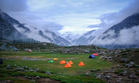 Small tents in a clearing amid cloud covered peaks.
