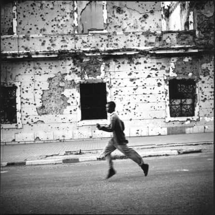 A boy runs past a bullet-scarred government building in Kuito, Angola.