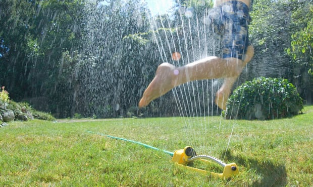 Boy jumping through water sprinkler