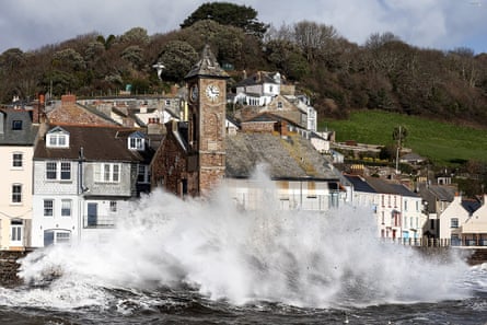 Waves splash up against the sea wall. A clock tower stands on the seafront surrounded by houses on a hill
