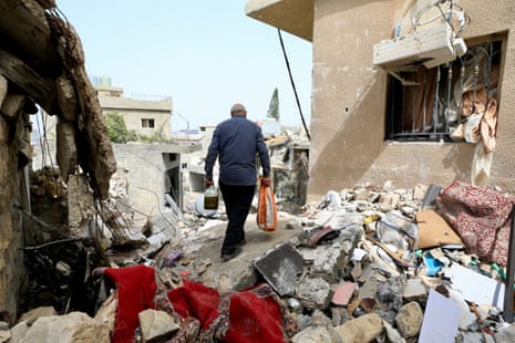 A man walks away through rubble and destruction with his back to the camera.