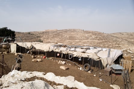 A fenced enclosure for sheep on a desert hillside, covered with a tarpaulin for shade 