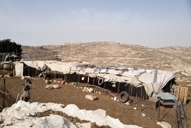 A fenced enclosure for sheep on a desert hillside, covered with a tarpaulin for shade