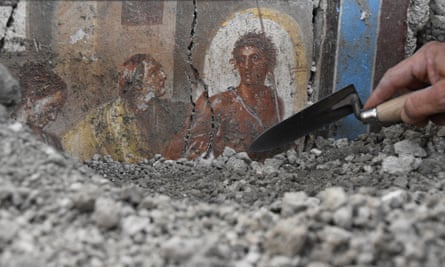 A person works with a trowel to uncover a fresco