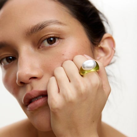 A model leans her face against her closed hand that is showcasing the Oliver Bonas Salma Faux Pearl Green Statement Ring in resin