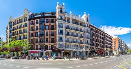 View of elegant, historic tall stone buildings in the Chamberí district around a road junction. There are shops on the ground floor and apartments with balconies above.