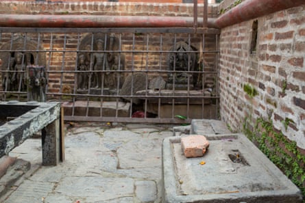 An empty stone dias in a courtyard, with a wall of metal bars protecting statues in arched alcoves