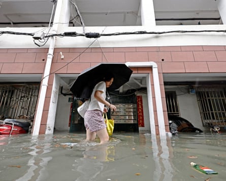A woman carrying an umbrella wades through thigh-deep grey water