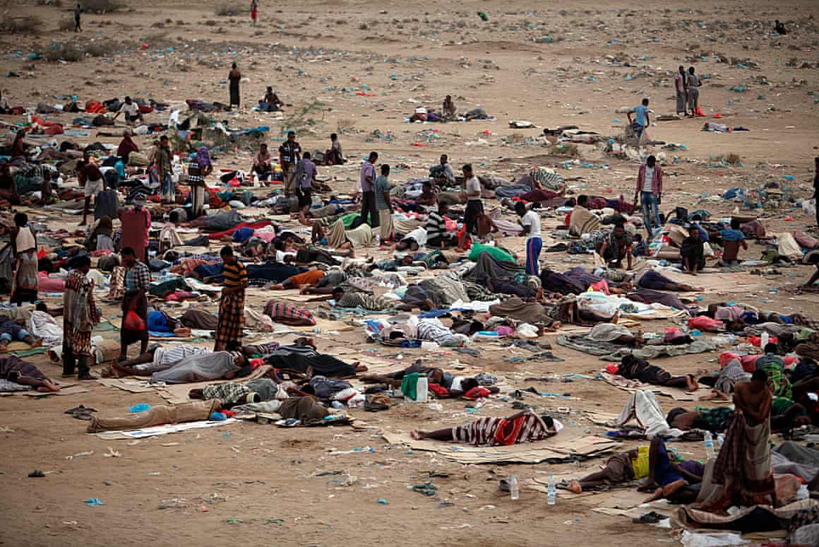 People lying and standing on blankets on sandy ground.