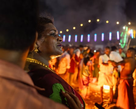A woman seen in profile next to a man whose face is turned from the camera. Behind them a crowd of festival goers is lit up by warm lights