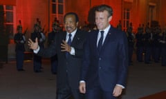 Emmanuel Macron smiles as he walks with a gesturing Paul Biya