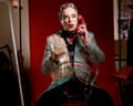 Julian Clary in dramatic makeup and a sequinned jacket holds a glittery red telephone to his ear