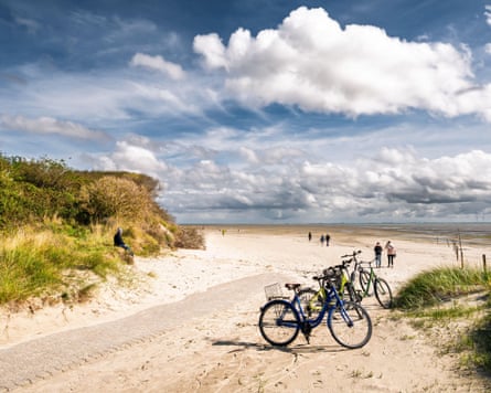 A sandy footpath with parked bicycles ending at the white sandy beach of Osterhook. People are walking on the beach in the distance.