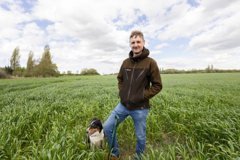 He stands in a field with a sheepdog at his feet