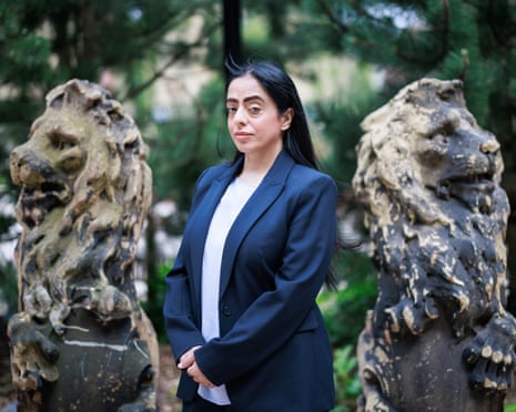 Arooj Shah in a navy blazer stands between two weathered stone lion statues in a garden