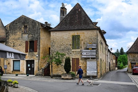 A man walks his dog past street signs in the centre of the village