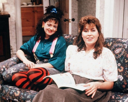 Two women sit on a sofa, in 1980s fashions