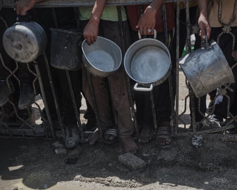 The hands of a queue of people can be seen holding large pans