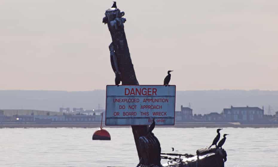 The mast of the wreck of the SS Richard Montgomery in the Thames displaying a warning sign, with Sheerness visible in the background.