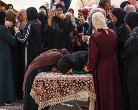 Two women bent over a coffin amid a crowd of mourners