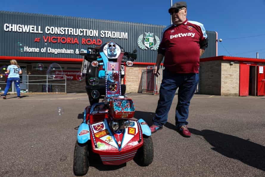 West Ham fan Trevor stands with his mobility scooter decorated with West Ham decals and blows bubbles.